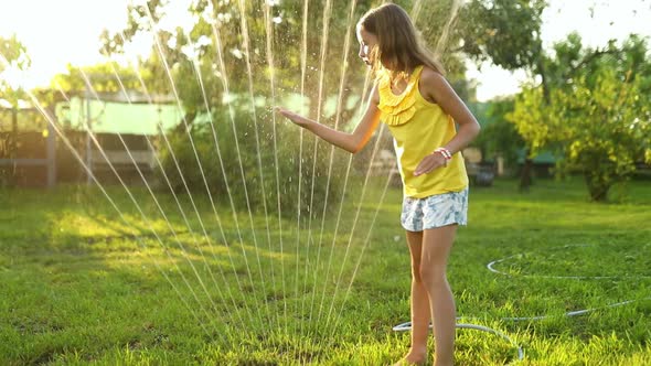 Happy kid girl playing with garden sprinkler run and jump