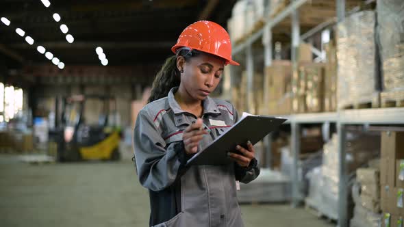 Black woman at the warehouse checks the availability of goods on the shelves alt