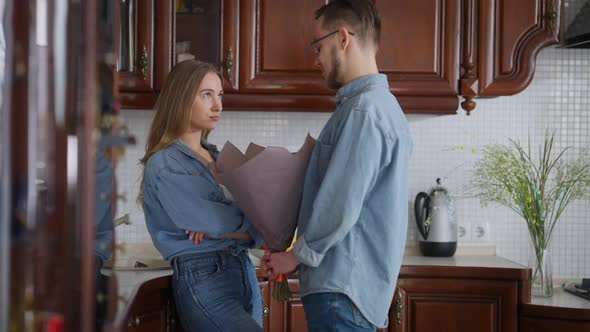 Portrait of Young Woman with Dissatisfied Facial Expression Standing in Kitchen As Man Entering alt