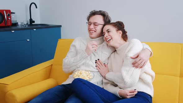 A Young Overjoyed Couple at Home Watching a Comedy Movie Laughing Loudly alt