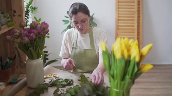 Professional Florist in a Green Apron Works with Flowers at the Table