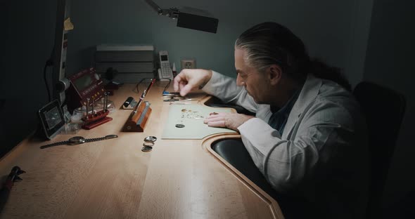 A watchmaker carefully removing the parts of a wristwatch he's repairing - wide shot alt