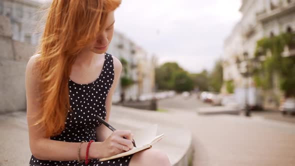 Young Cute Caucasian Redhead Girl Writing Notes Wearing Black Polka Dot Dress alt