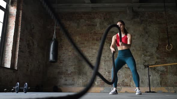 Young woman exercising with battle ropes at the gym.