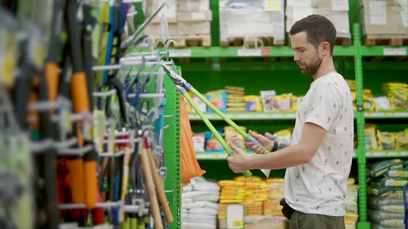 Adult Man is Watching and Trying Pruning Shear in a Hardware Store alt