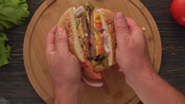 Top View of the Male Hands Opening Burger with Meat Cutlet Cut in Two Halves alt