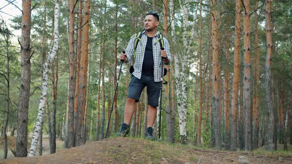 Slow Motion of Hiker Standing in Forest Then Walking with Poles on Summer Day alt