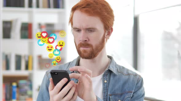Redhead Beard Designer Using Smartphone, Flying Emojis, Smileys and Likes alt