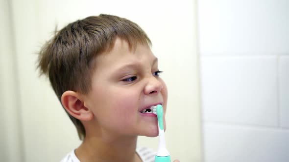 close up view of cute caucasian boy brushing his teeth with electric brush in bathroom