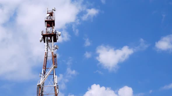 Telecommunication Tower With Antennas And Repeaters Against Blue Sky And Clouds alt