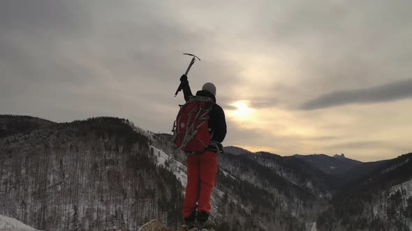 The Silhouette of a Young Male Climber Standing on Top of a Mountain and Holding Up an Ice Axe