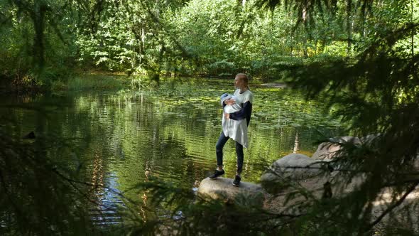 woman cradles a baby on the shore of a forest lake