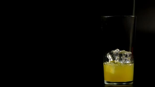 Orange Juice Is Poured Into A Tall Glass With Ice On A Black Background
