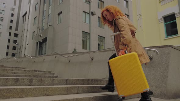 Young European Woman Enters the Business Center with a Yellow Suitcase alt