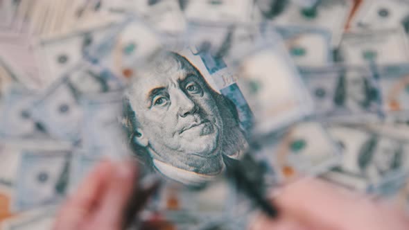 Lot of One Hundred Dollars Bills Inspecting Under Magnifying Glass alt
