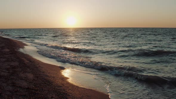 Aerial View Above Water of Nesting Small Waves Against Sandy Shore Against the Backdrop of Sunset alt