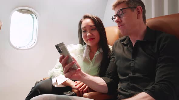 Happy young couple in love traveling see smartphone and smile together on the airplane