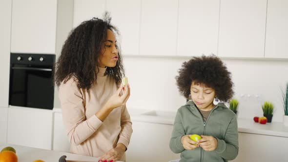 Mixed Race Mother and Son Eating Fruit in the Kitchen alt