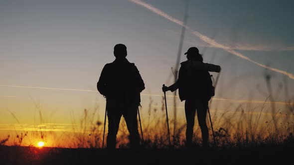 Silhouettes of Two Hikers with Backpacks Enjoying Sunset View From Top of a Mountain. Enjoying the alt