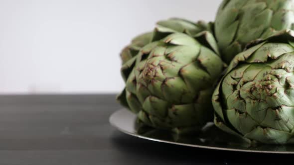 Whole Fresh Artichokes on Plate on Black Table alt