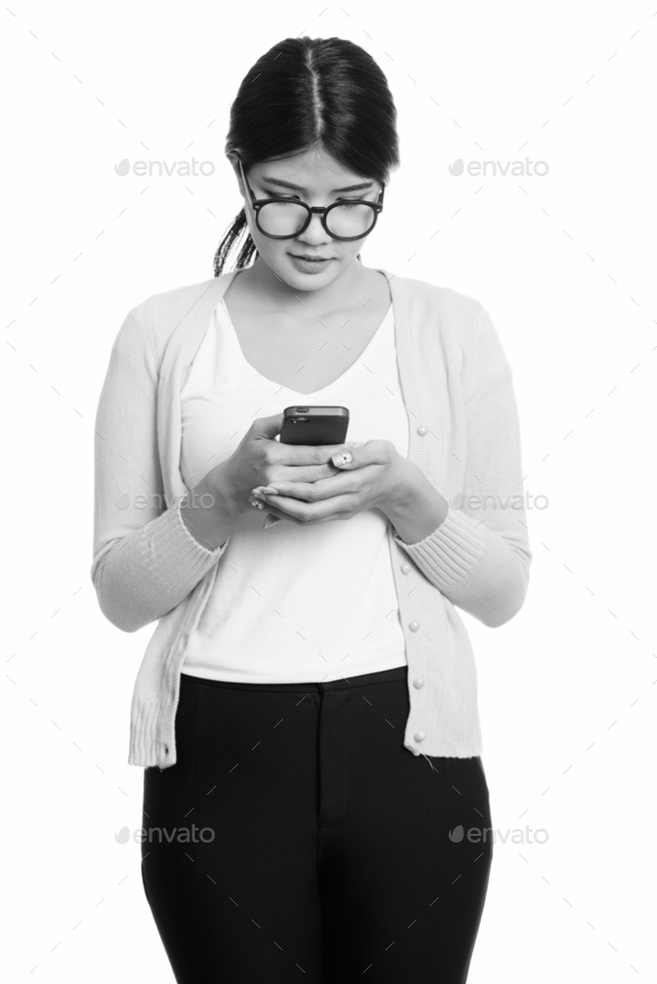 Studio shot of young Asian nerd woman using mobile phone