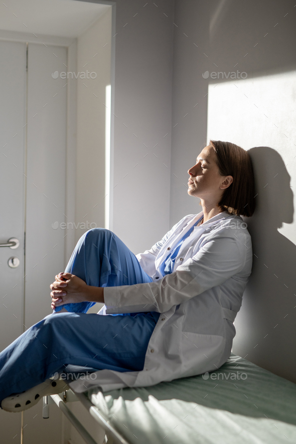 Young exhausted nurse of covid hospital in uniform resting on medical cart