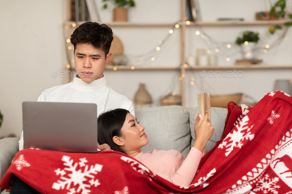 Couple Reading Book And Watching Movie On Laptop At Home