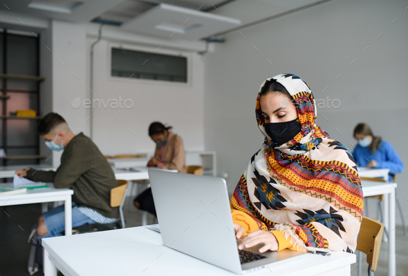 Islamic student with face mask at desks at college or university, coronavirus concept.