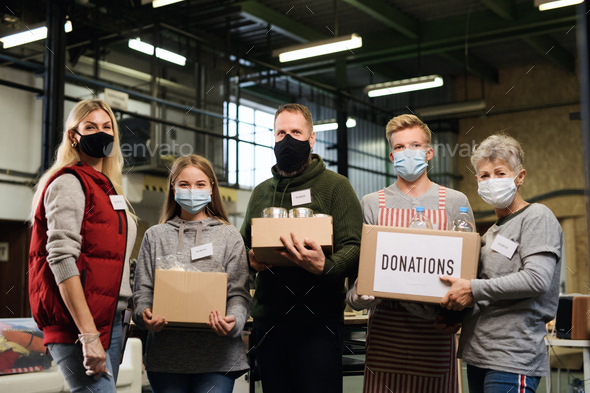 Group of volunteers looking at camera in community charity donation center, coronavirus concept.