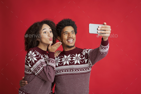 Selfie of couple in love. Happy african american man holds smartphone, lady blowing kiss or make