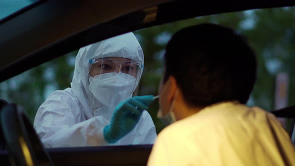 doctor in PPE suit test coronavirus(covid-19) to man in car by nasal swab cotton, drive thru test
