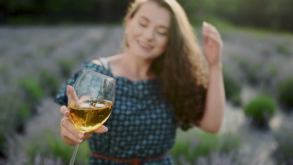 Adult Brunette Curly Woman is Holding Glass with Wine and Lavander at Winetasting Viewing Color