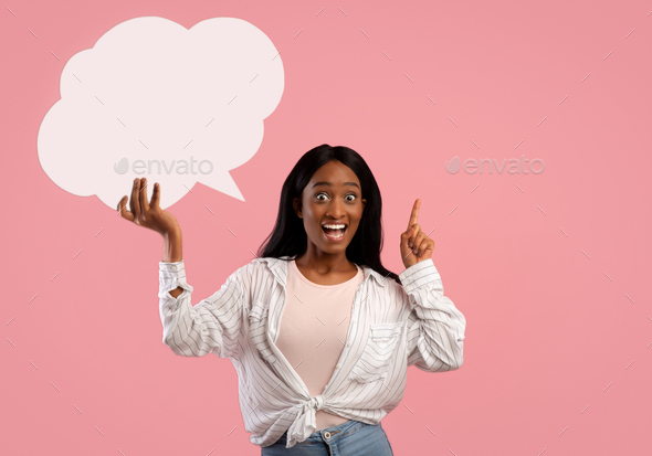 Excited black lady holding empty speech bubble and pointing her finger up on pink studio background