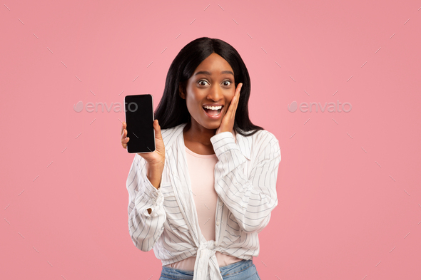 Excited black lady shouting OMG and showing cellphone with blank screen on pink background, mockup