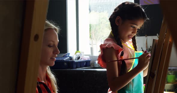 Teacher assisting schoolgirl in drawing class alt