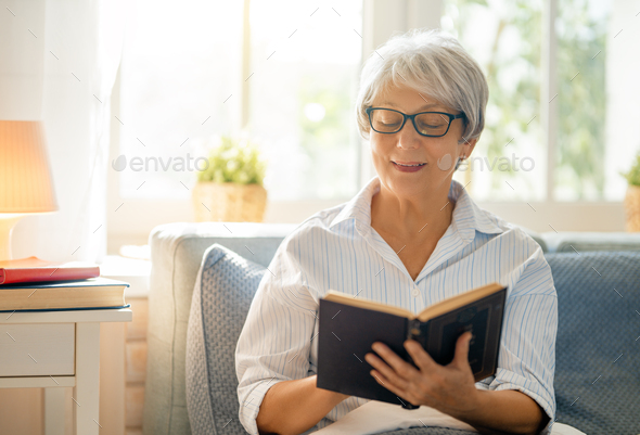 Joyful beautiful senior woman is reading sitting on the bed at home.