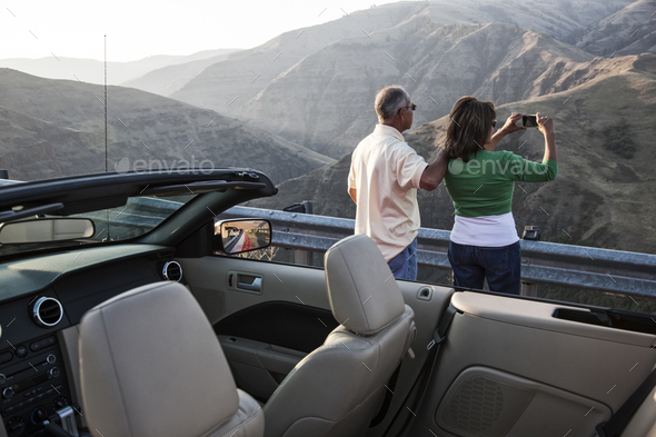 An Hispanic senior couple taking a picture of the scenery from a highway stop - Stock Photo - Images