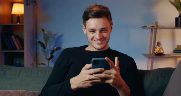 Cheerful Millennial Man Communicating with Friends in Social Networks and Laughing While Getting alt