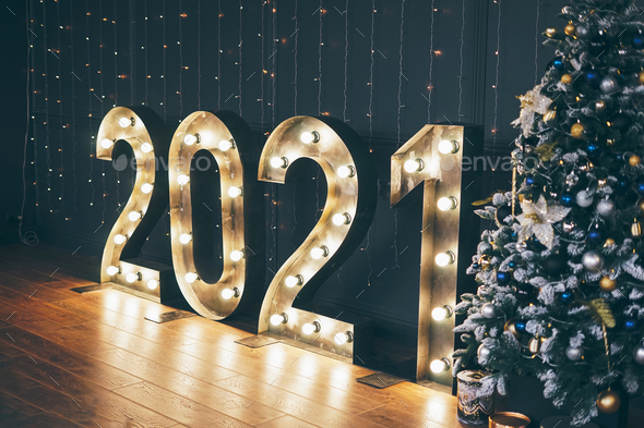 Glowing numbers 2021 on a dark wall background, decorated Christmas tree - Stock Photo - Images