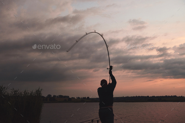 Silhouette of fisherman throws a fishing pole into the lake at sunset Stock  Photo by mstandret