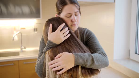 Young Mother Hugging and Consoling Upset Crying Daughter on Kitchen alt