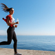 Side view of attractive and healthy fitness woman running along the seaside  promenade. Girl jogging Stock Photo by benzoix