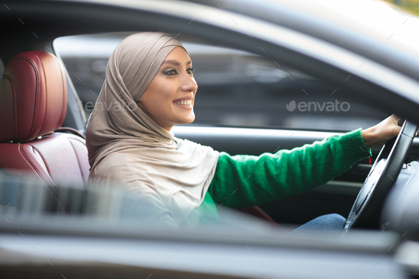 Smiling muslim woman driving her new car in urban city