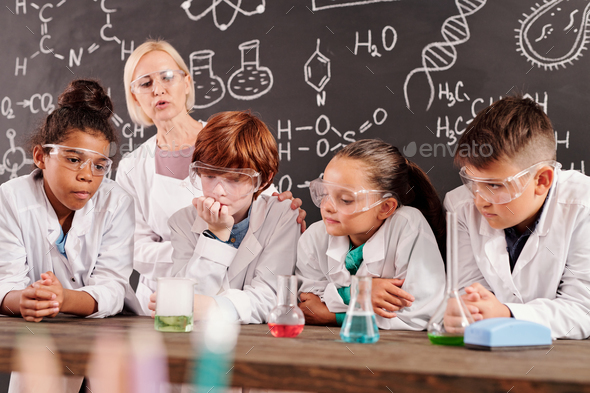 Schoolkids watching different reactions in glass tubes with chemical compounds