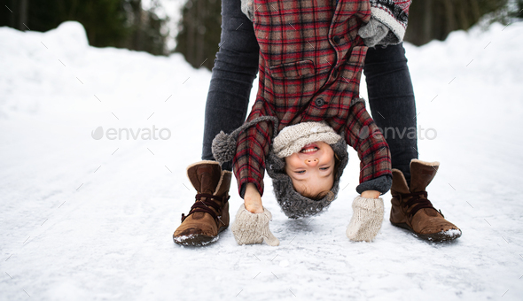 Unrecognizable mother holding small daughter upside down in winter nature.