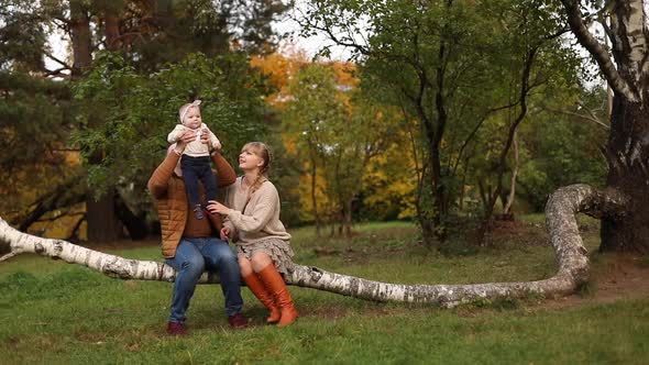 Young Parents Walking with Daughter in Forest in Autumn