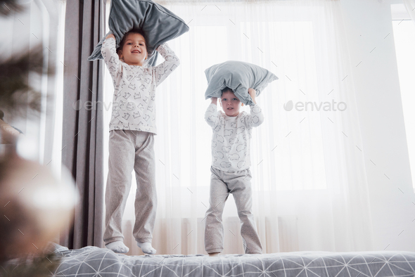 Kids playing in parents bed. Children wake up in sunny white bedroom. Boy and girl play in matching