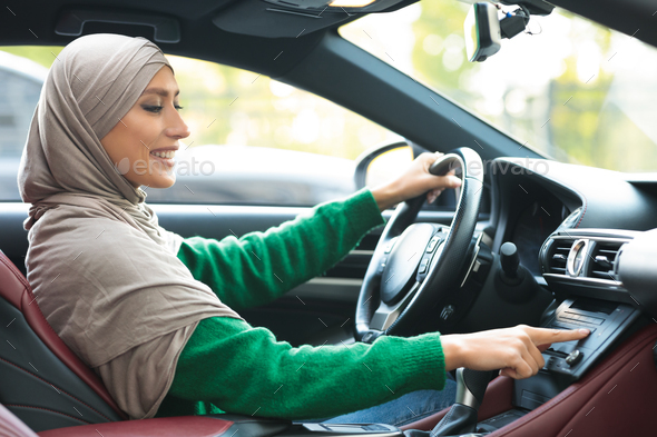 Cheerful muslim woman driving car, using dashboard