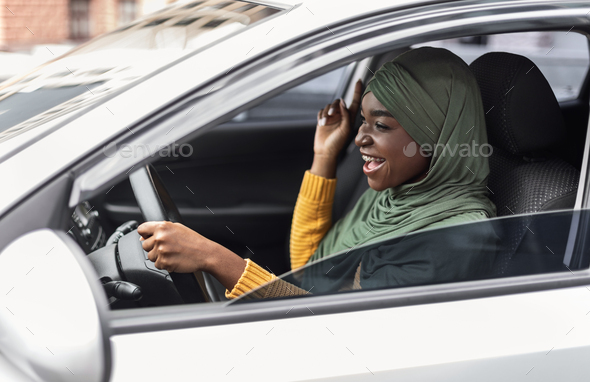 Driving Fun. Cheerful black muslim woman listening music and singing in car