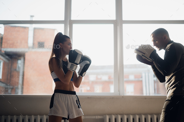 A man and a woman sparring partners train in the fighters training hall in boxing gloves with paws